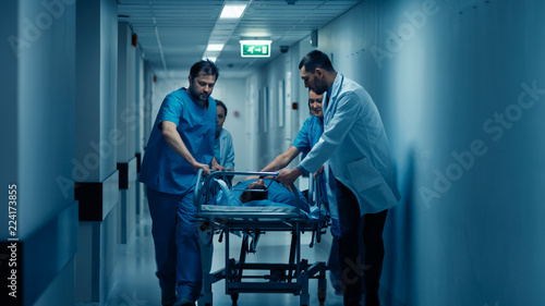 Emergency Department: Doctors, Nurses and Paramedics Run and Push Gurney / Stretcher with Seriously Injured Patient towards the Operating Room. Modern Hospital with Professional Staff. photo
