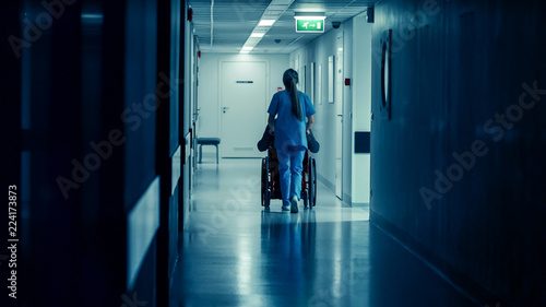 Shot of the Female Nurse Moving Patient in the Wheelchair Through the Hospital Corridor. Doing Procedures. Bright Modern Hospital with Friendly Staff.