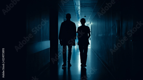 Medical Staff Silhouettes Walk in Dark Part of the Hospital Corridor. © Gorodenkoff