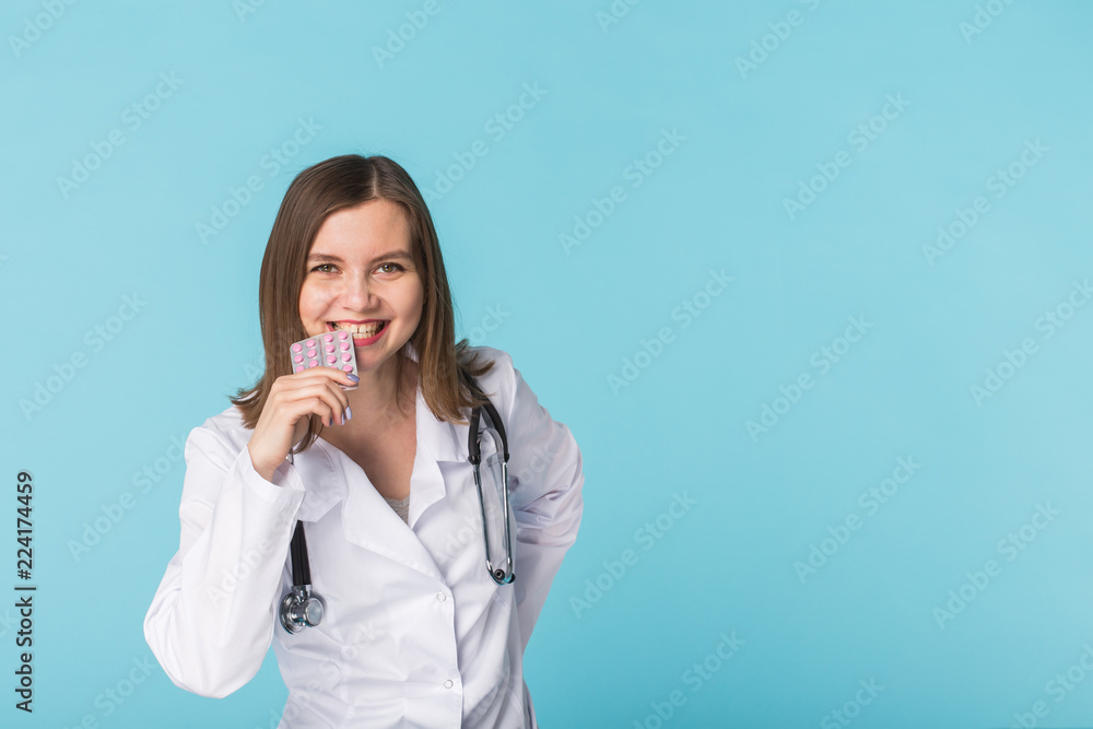 Young female doctor tasting pack of pills on blue background with copy space Young female doctor tasting pack of pills on blue background with copy space
