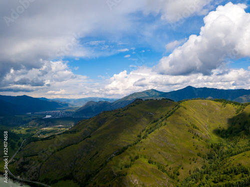 Aerial view to landscape of green valley flooded with light with lush green grass   covered with stone and hills  a fresh summer day under a blue sky with white clouds and sun rays in Altai mountains