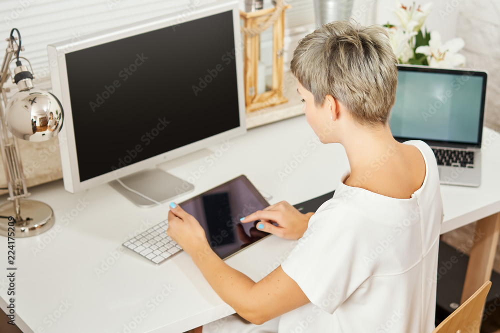 beautiful business woman in a white dress sitting at a desk and works on a tablet in a home office beautiful business woman in a white dress sitting at a desk and works on a tablet in a home office