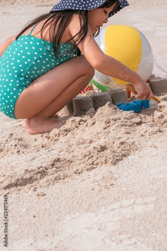 little asian girl playing with sand at the tropical beach in summer.