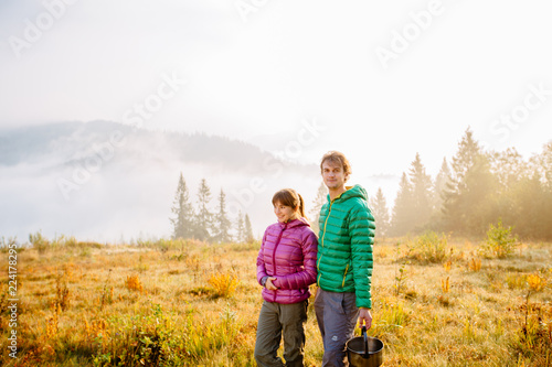Autumn nature lifestyle man and woman meet morning together on camping travel park with fog on background. Hiking couple wearing green and purple down jacket enjoying fall season landscape.