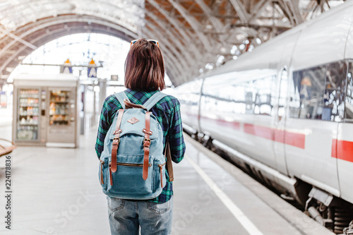 A young tourist girl with backpack waits for train on railway station