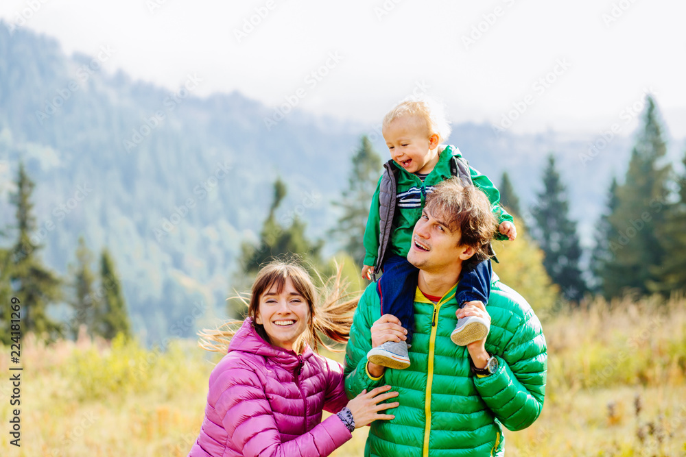 Story of happy family mother, father and toddler son wearing colorful duck jacket are playing togtether while traveling on Carpathain mountains. Travel with children, tourism and sport concept.