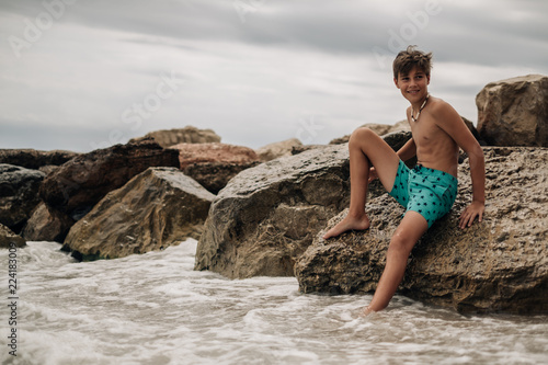 Smiling boy sitting on the beach rock
