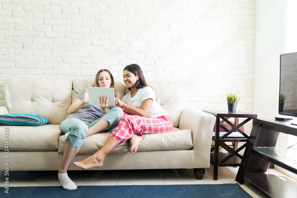 Females In Pajamas Using Digital Tablet While Relaxing On Sofa