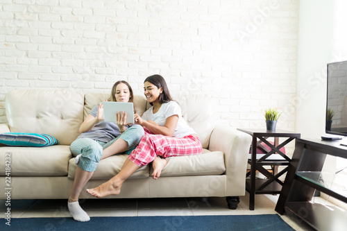 Females In Pajamas Using Digital Tablet While Relaxing On Sofa