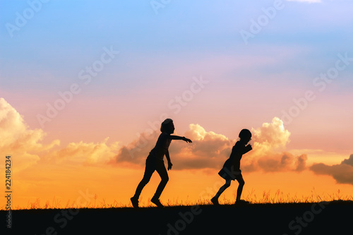 Kids running on meadow at sunset time silhouette