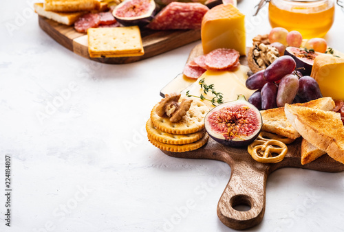 Cheese plate served with grapes, jam, figs, crackers and nuts on a white background. Copy space.