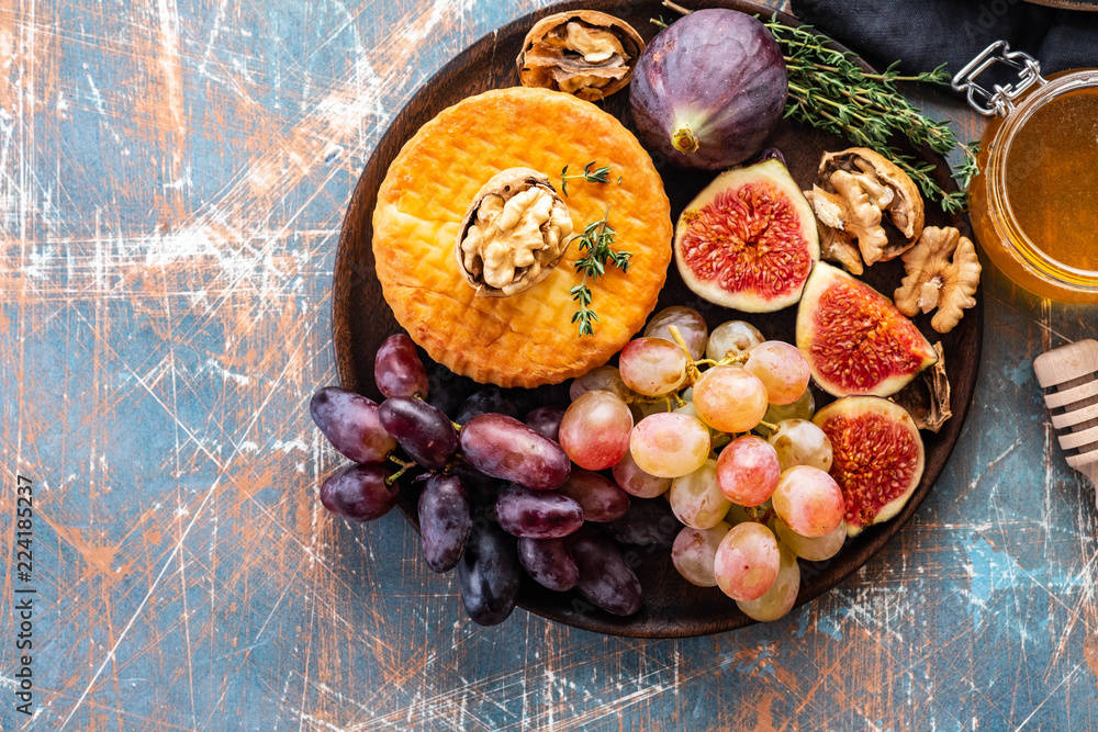 Cheese plate served with grapes, jam, figs, honey and nuts on a rustic background. Copy space.