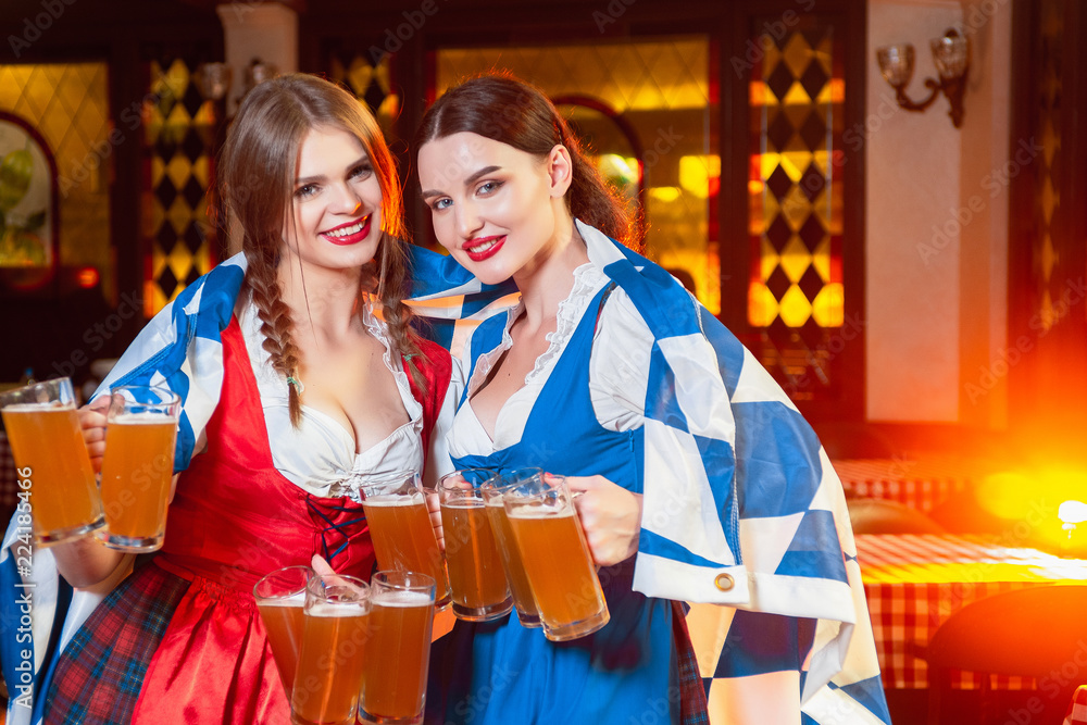 Young beautiful girls with glasses of beer in hands under the flag oktoberfest.