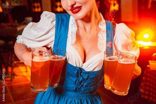 Young beautiful girl holds four glasses of beer in hands at celebration of oktoberfest. Beer glasses on the background of the female breast.
