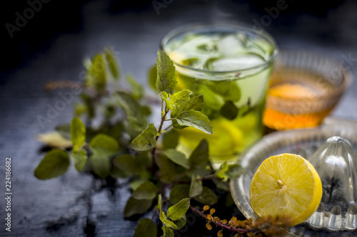 Close up of Herabal drink or Basil lemonade in a transparent glass with raw basil,raw honey,ice cubes and lemon juice on wooden surface,Helps in curing cough,stress,headache,etc.