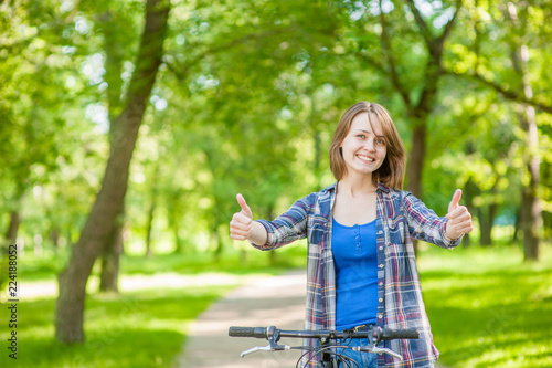 Happy young beautiful woman with bike showing thumbs up. Space for text