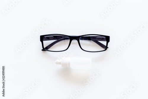 Eye health. Glasses with transparent optical lenses and eye drops on white background top view copy space closeup photo