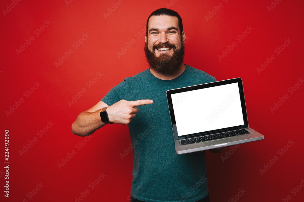 Smiling bearded man pointing at white laptop screen, copyspace Smiling bearded man pointing at white laptop screen, copyspace