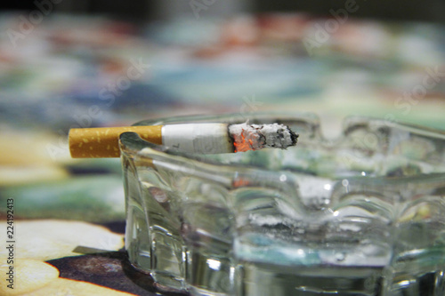 Glass ashtray with a burning cigarette on the table photo