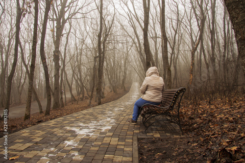 Lonely adult woman sitting in autumn park in mysty morning photo