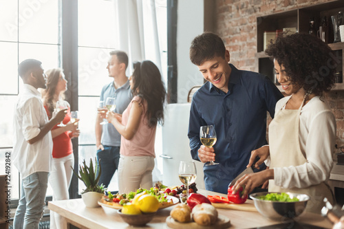 Multiethnic couple preparing dinner in kitchen with friends