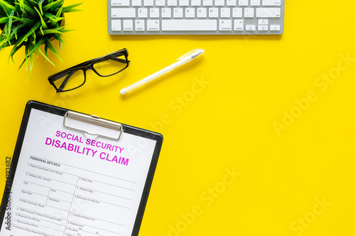 Social security. Disability claim form near glasses on office desk on yellow background top view copy space