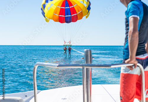 Happy couple Parasailing in Dominicana beach in summer. Couple under parachute hanging mid air. Having fun. Tropical Paradise. Positive human emotions, feelings, family, children, travel, vacation. 