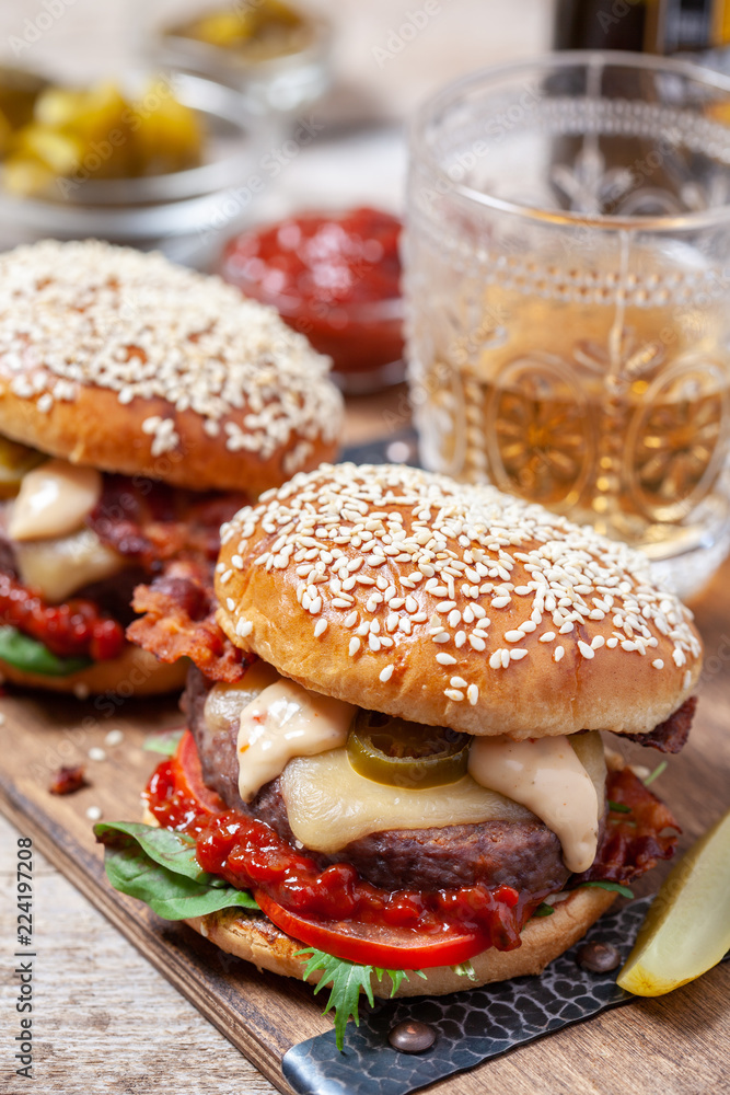 Two cheeseburgers on sesame buns with jalapeno on a rustic wood table
