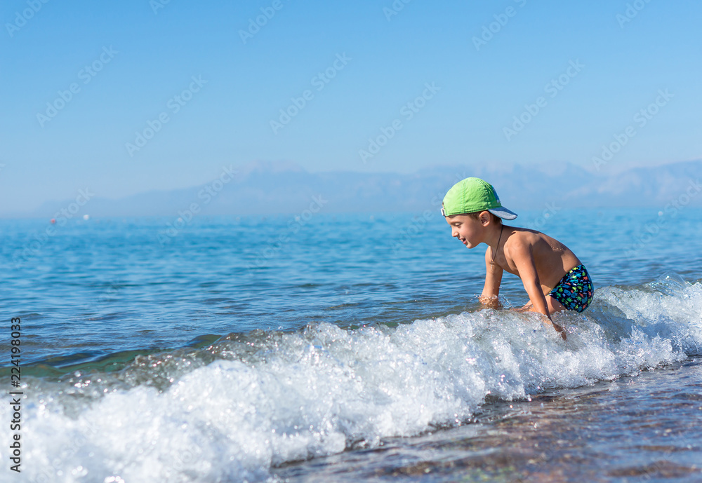 Smiling little baby boy in green baseball cap playing in the sea. Positive human emotions, feelings, joy.