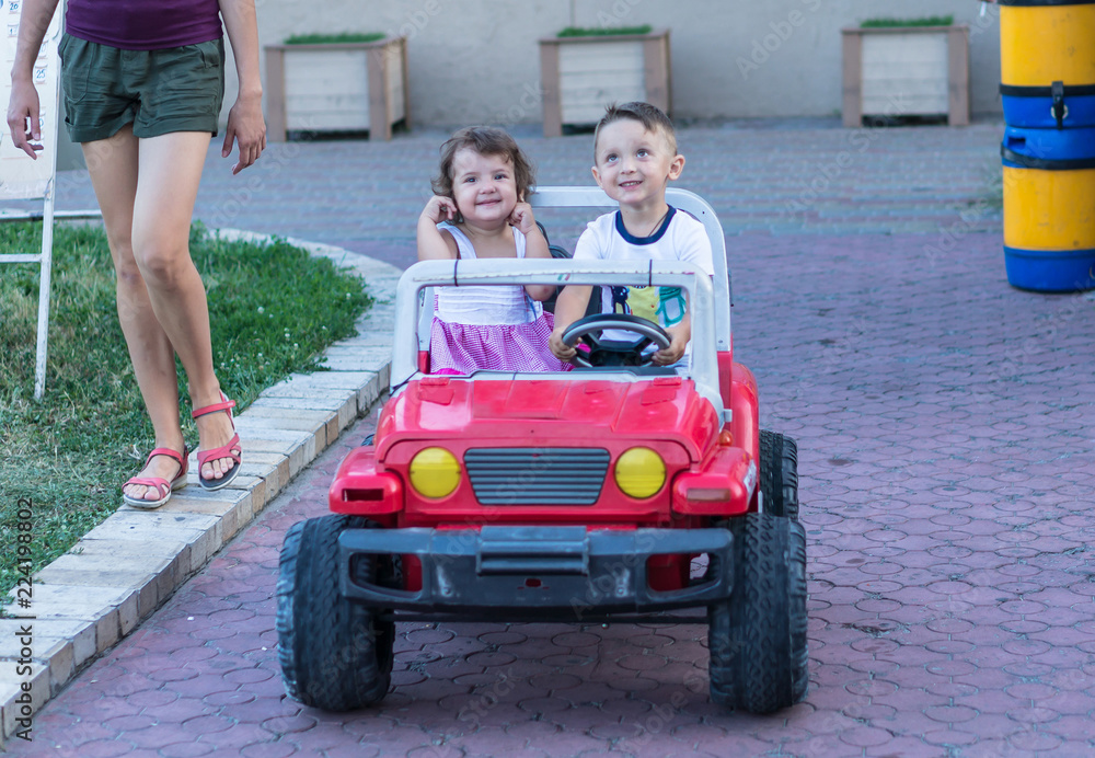 Smiling little brother and sister driving by toy car. Portrait of happy little kids on the street. Funny cute children making vacations and enjoying summer. Healthy lifestyle. Positive human emotions. Smiling little brother and sister driving by toy car. Portrait of happy little kids on the street. Funny cute children making vacations and enjoying summer. Healthy lifestyle. Positive human emotions.