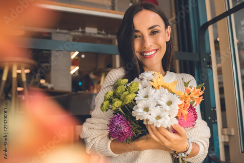 Photo portrait of smiling young woman holding colorful bouquet from various flowers in