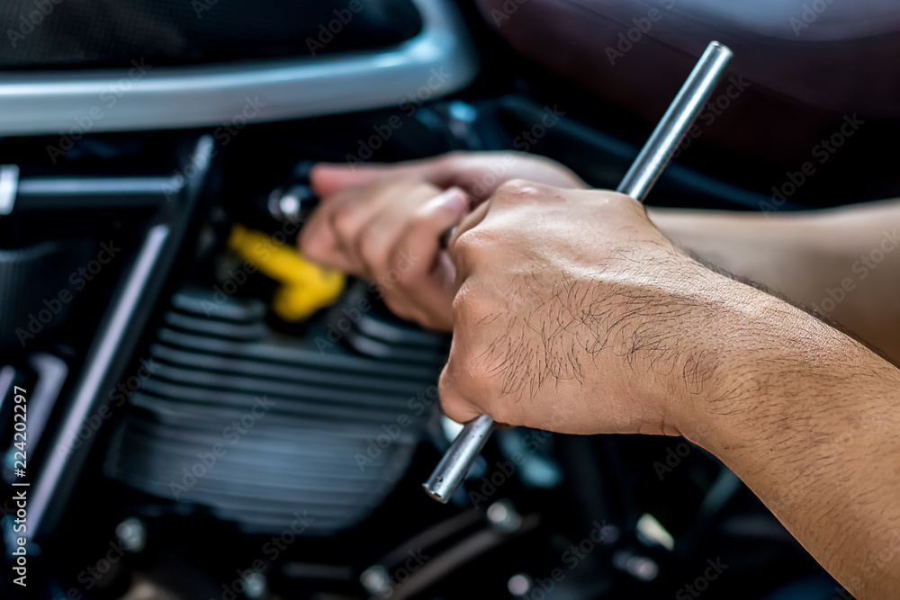 Image is close up. People holding hand are repairing a motorcycle Use a wrench and a screwdriver to work.