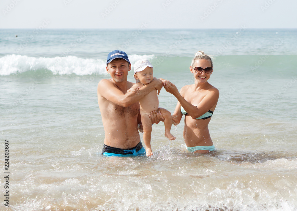 Young family with little baby boy jumping on the waves in the sea Young family with little baby boy jumping on the waves in the sea