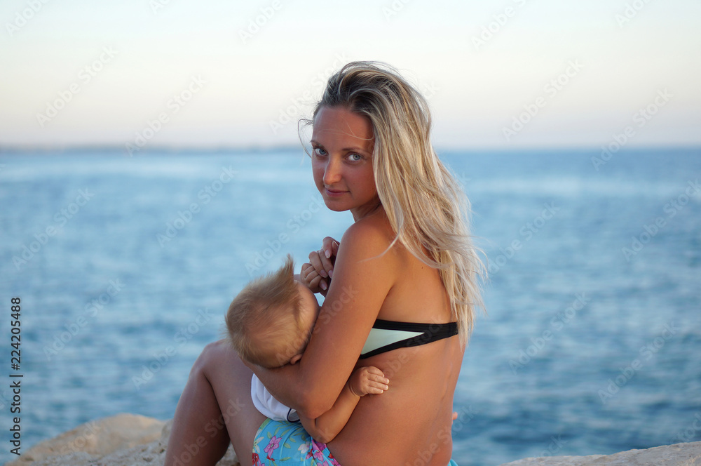Mother breastfeeding baby on the beach at sunset near the sea Mother breastfeeding baby on the beach at sunset near the sea