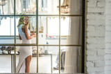 Portrait of a beautiful young woman in a white dress through the window.
