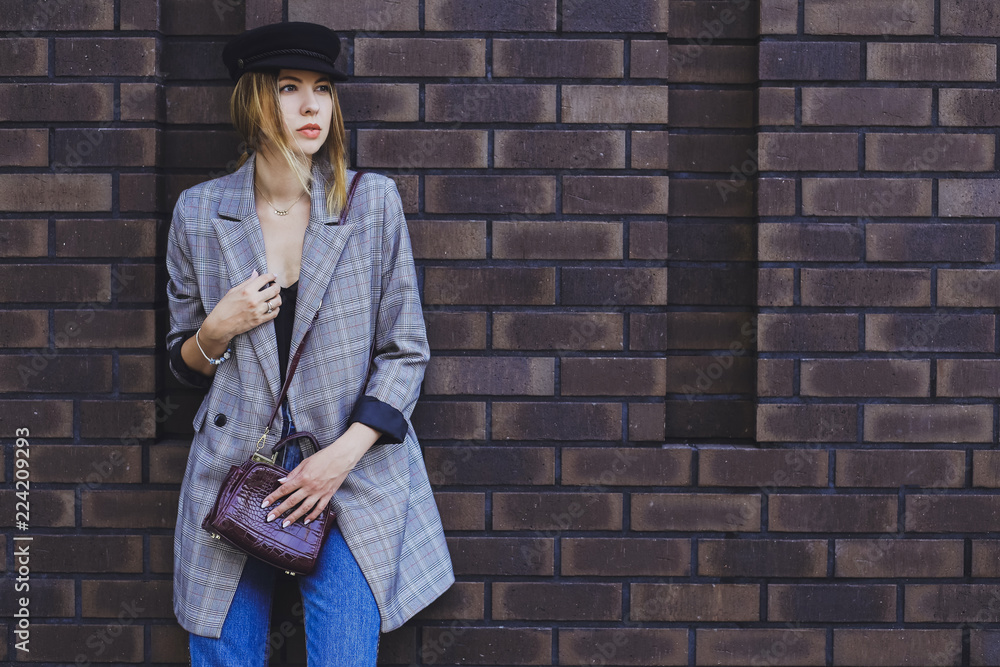 Young beautiful girl in a jacket, jeans and hat on a brick wall background Young beautiful girl in a jacket, jeans and hat on a brick wall background