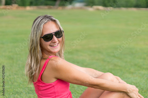 Attractive young smiling beautiful curly blonde hair slim girl fashion portrait in pink T-shirt posing looking away calm look, in background green grass meadow. Healthy woman lifestyle concept.