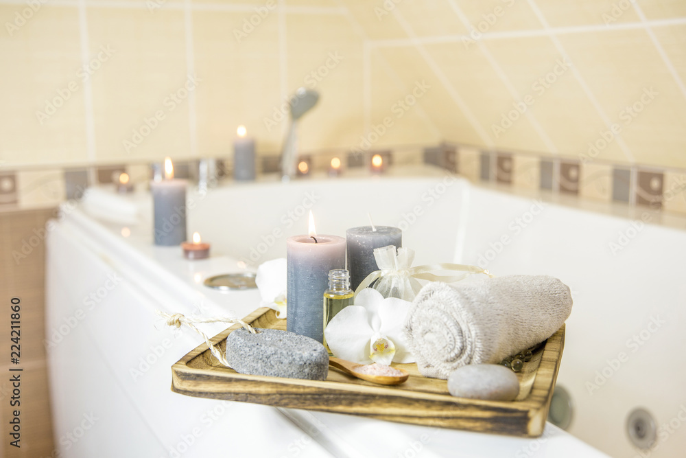 Candles burning and spa essentials on wooden tray in bathroom, essential oil, bath salt on wooden spoon, pumice stone, towel, sea stone, white orchids. Spa products set conception. Candles burning and spa essentials on wooden tray in bathroom, essential oil, bath salt on wooden spoon, pumice stone, towel, sea stone, white orchids. Spa products set conception.