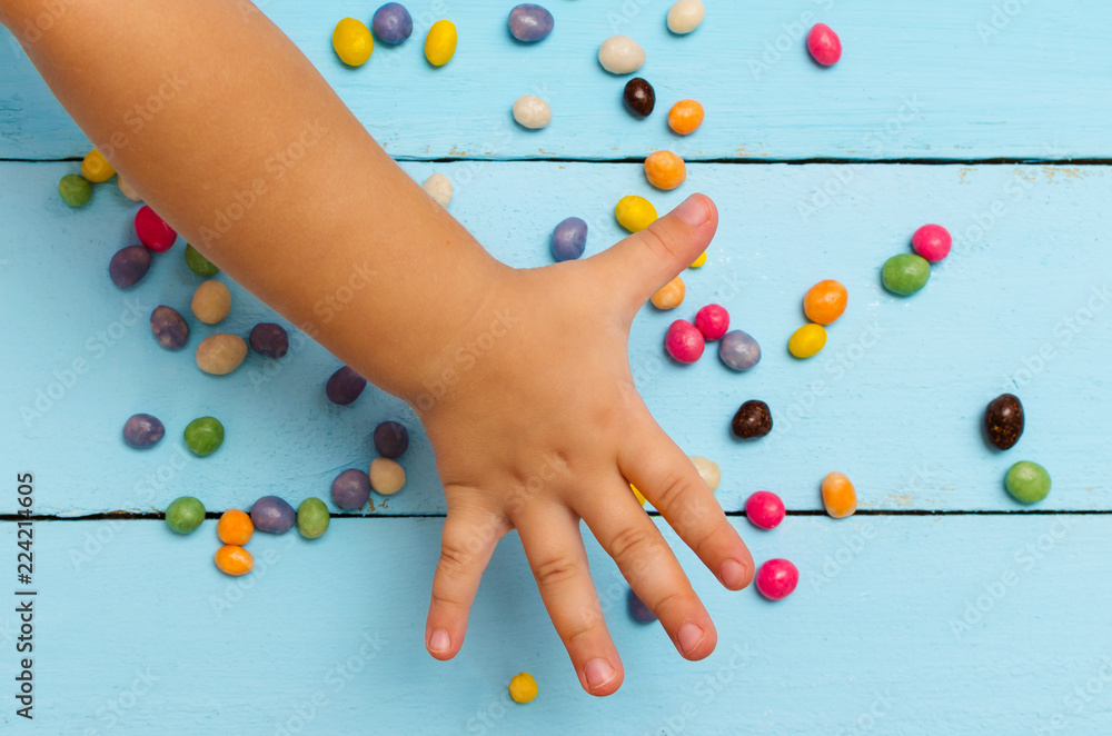 The child pulls his hand to the colored candy on the blue table The child pulls his hand to the colored candy on the blue table