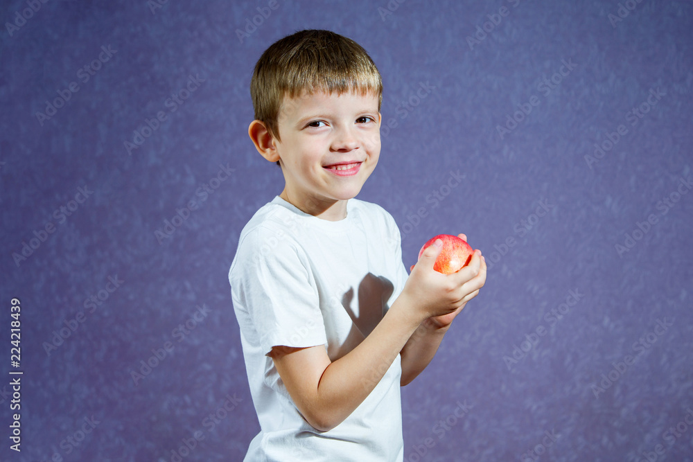 Little boy in a white T-shirt on a purple background holding a red apple and laughing Little boy in a white T-shirt on a purple background holding a red apple and laughing