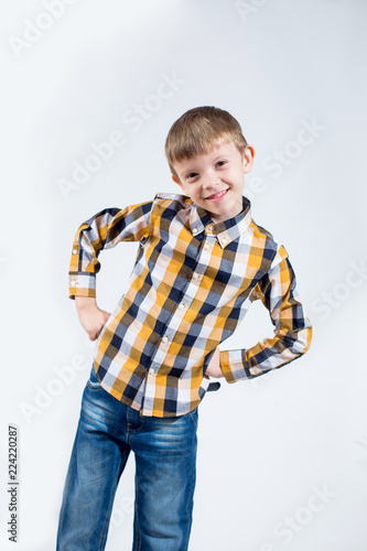 Little boy in a plaid shirt on a white background stands and folded his arms on his hips