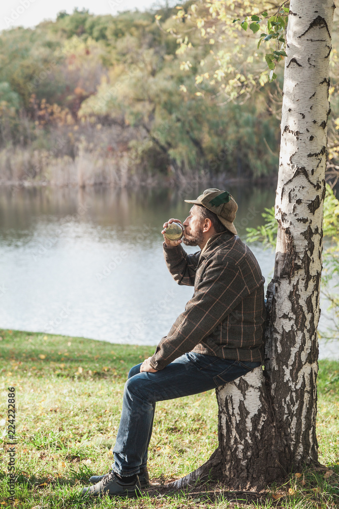 man with beard in plaid jacket drinks from round flask man with beard in plaid jacket drinks from round flask