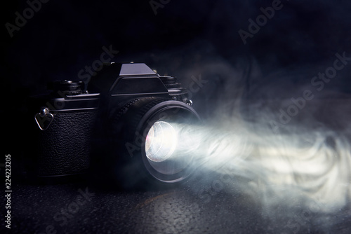 old camera with a ray of light from the lens in the smoke on a black background