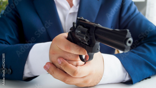 Closeup photo fo businessman in suit sitting in armchair and aiming with revolver