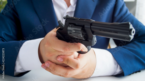 Closeup photo of businessman in suit sitting in office and holding revolver