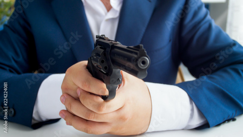 Closeup photo of man in suit sitting in armchair at office and aiming with gun
