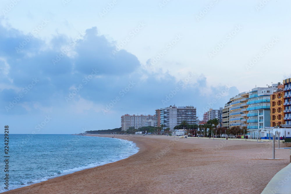 Coast of sandy beach and architecture of Spanish beach resort Blanes in summertime. Costa Brava, Catalonia. Tourists relax on beach and walk along the coastal promenade. Spain Coast of sandy beach and architecture of Spanish beach resort Blanes in summertime. Costa Brava, Catalonia. Tourists relax on beach and walk along the coastal promenade. Spain
