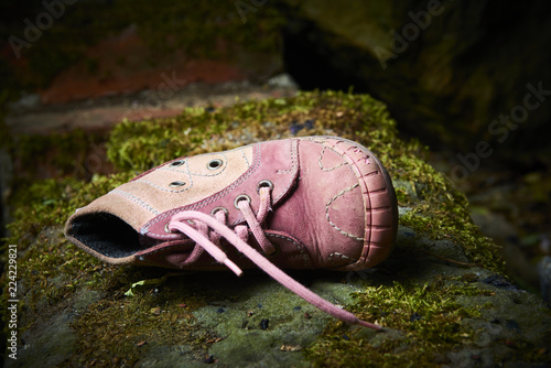 Photos Abandoned baby shoe lying on an old stone covered with moss