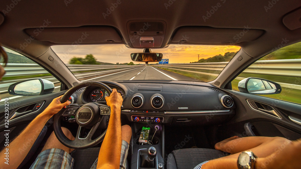 Driver's hands on a steering wheel of a car and woman in the passenger seat. Road trip on the Italians road at evening time.