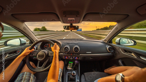 Driver's hands on a steering wheel of a car and woman in the passenger seat. Road trip on the Italians road at evening time. © pozdeevvs
